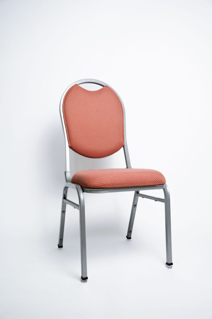 Elegância e Robustez para Grandes Eventos A Cadeira Ruby CR da Tomberlin foi projetada para atender às altas exigências do mercado de hotéis e eventos. Com um encosto de design sofisticado, ela garante não apenas o conforto visual e físico dos convidados, mas também um excelente retorno sobre o investimento devido à sua durabilidade superior.Estrutura de Alta Performance Fabricada com estrutura reforçada em aço carbono, a cadeira recebe um exclusivo tratamento nanocerâmico e acabamento em pintura eletrostática a pó. Esses processos garantem máxima proteção contra o desgaste diário. Para projetos que exigem maior leveza no manuseio, a estrutura pode ser substituída por alumínio, o que reduz o peso da peça em cerca de 2 kg.Conforto Prolongado Pensando no bem-estar durante palestras, casamentos e convenções, o assento e o encosto são desenvolvidos com espuma injetada e revestidos em tecido 100% poliéster.Armazenamento Inteligente e Diferenciais TomberlinEmpilhamento Seguro: Sistema estrutural inteligente que garante um grande número de cadeiras empilhadas com segurança e praticidade.Protetor Lateral: Todos os modelos possuem protetores em plástico injetado nas laterais, desenhados especificamente para evitar danos ao chassi durante o empilhamento.Sapatas em Policarbonato: O policarbonato é mais resistente a atritos e impactos, garantindo mais durabilidade à peça e protegendo o piso do seu espaço.