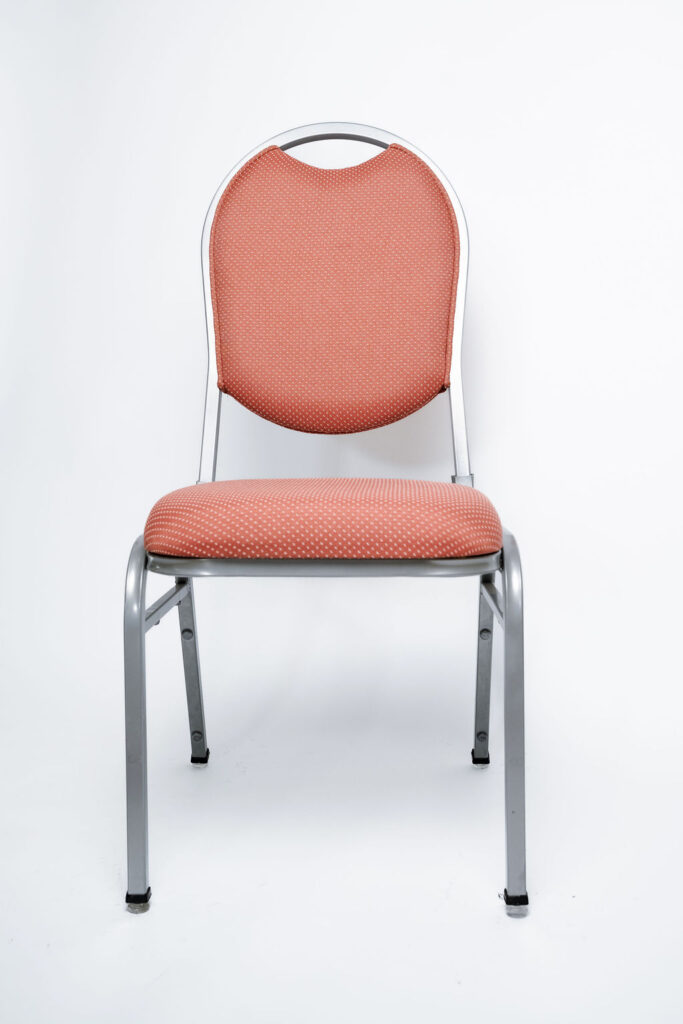 Elegância e Robustez para Grandes Eventos A Cadeira Ruby CR da Tomberlin foi projetada para atender às altas exigências do mercado de hotéis e eventos. Com um encosto de design sofisticado, ela garante não apenas o conforto visual e físico dos convidados, mas também um excelente retorno sobre o investimento devido à sua durabilidade superior.Estrutura de Alta Performance Fabricada com estrutura reforçada em aço carbono, a cadeira recebe um exclusivo tratamento nanocerâmico e acabamento em pintura eletrostática a pó. Esses processos garantem máxima proteção contra o desgaste diário. Para projetos que exigem maior leveza no manuseio, a estrutura pode ser substituída por alumínio, o que reduz o peso da peça em cerca de 2 kg.Conforto Prolongado Pensando no bem-estar durante palestras, casamentos e convenções, o assento e o encosto são desenvolvidos com espuma injetada e revestidos em tecido 100% poliéster.Armazenamento Inteligente e Diferenciais TomberlinEmpilhamento Seguro: Sistema estrutural inteligente que garante um grande número de cadeiras empilhadas com segurança e praticidade.Protetor Lateral: Todos os modelos possuem protetores em plástico injetado nas laterais, desenhados especificamente para evitar danos ao chassi durante o empilhamento.Sapatas em Policarbonato: O policarbonato é mais resistente a atritos e impactos, garantindo mais durabilidade à peça e protegendo o piso do seu espaço.