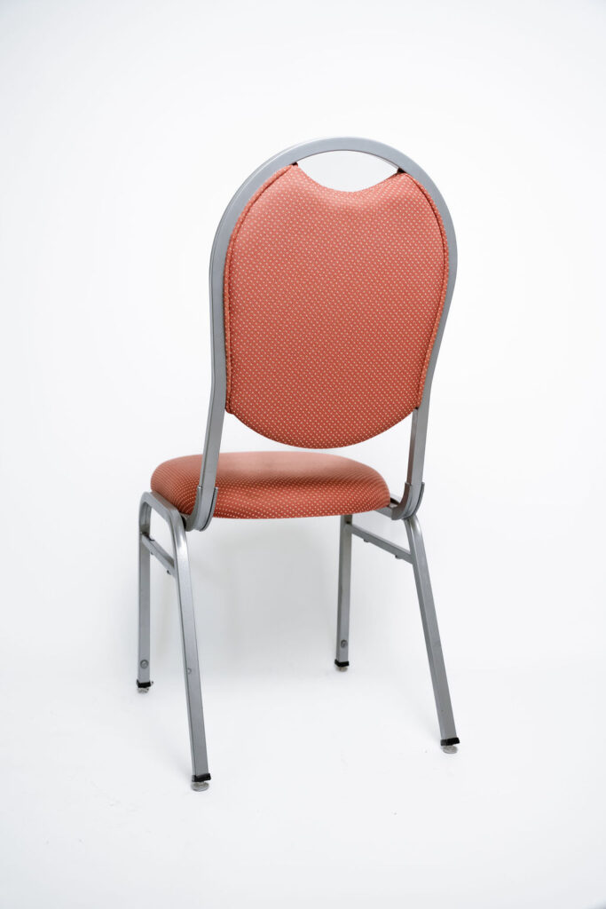 Elegância e Robustez para Grandes Eventos A Cadeira Ruby CR da Tomberlin foi projetada para atender às altas exigências do mercado de hotéis e eventos. Com um encosto de design sofisticado, ela garante não apenas o conforto visual e físico dos convidados, mas também um excelente retorno sobre o investimento devido à sua durabilidade superior.Estrutura de Alta Performance Fabricada com estrutura reforçada em aço carbono, a cadeira recebe um exclusivo tratamento nanocerâmico e acabamento em pintura eletrostática a pó. Esses processos garantem máxima proteção contra o desgaste diário. Para projetos que exigem maior leveza no manuseio, a estrutura pode ser substituída por alumínio, o que reduz o peso da peça em cerca de 2 kg.Conforto Prolongado Pensando no bem-estar durante palestras, casamentos e convenções, o assento e o encosto são desenvolvidos com espuma injetada e revestidos em tecido 100% poliéster.Armazenamento Inteligente e Diferenciais TomberlinEmpilhamento Seguro: Sistema estrutural inteligente que garante um grande número de cadeiras empilhadas com segurança e praticidade.Protetor Lateral: Todos os modelos possuem protetores em plástico injetado nas laterais, desenhados especificamente para evitar danos ao chassi durante o empilhamento.Sapatas em Policarbonato: O policarbonato é mais resistente a atritos e impactos, garantindo mais durabilidade à peça e protegendo o piso do seu espaço.