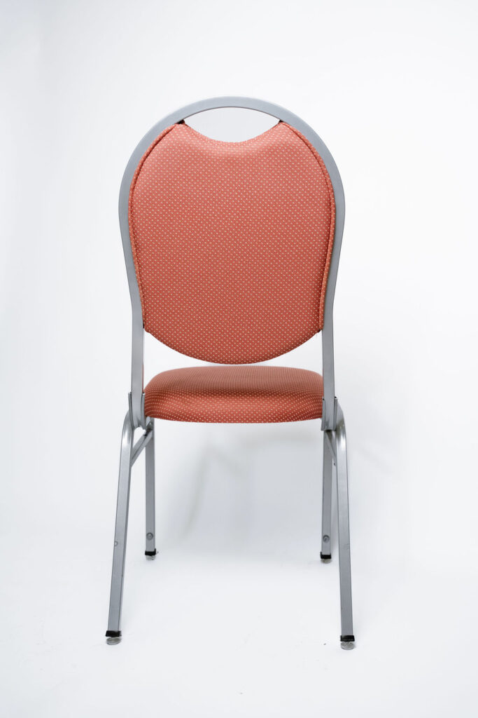 Elegância e Robustez para Grandes Eventos A Cadeira Ruby CR da Tomberlin foi projetada para atender às altas exigências do mercado de hotéis e eventos. Com um encosto de design sofisticado, ela garante não apenas o conforto visual e físico dos convidados, mas também um excelente retorno sobre o investimento devido à sua durabilidade superior.Estrutura de Alta Performance Fabricada com estrutura reforçada em aço carbono, a cadeira recebe um exclusivo tratamento nanocerâmico e acabamento em pintura eletrostática a pó. Esses processos garantem máxima proteção contra o desgaste diário. Para projetos que exigem maior leveza no manuseio, a estrutura pode ser substituída por alumínio, o que reduz o peso da peça em cerca de 2 kg.Conforto Prolongado Pensando no bem-estar durante palestras, casamentos e convenções, o assento e o encosto são desenvolvidos com espuma injetada e revestidos em tecido 100% poliéster.Armazenamento Inteligente e Diferenciais TomberlinEmpilhamento Seguro: Sistema estrutural inteligente que garante um grande número de cadeiras empilhadas com segurança e praticidade.Protetor Lateral: Todos os modelos possuem protetores em plástico injetado nas laterais, desenhados especificamente para evitar danos ao chassi durante o empilhamento.Sapatas em Policarbonato: O policarbonato é mais resistente a atritos e impactos, garantindo mais durabilidade à peça e protegendo o piso do seu espaço.